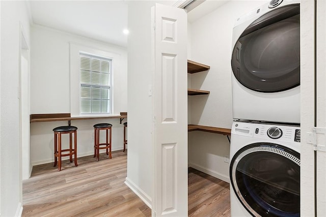 clothes washing area with laundry area, wood finished floors, stacked washer and clothes dryer, and baseboards