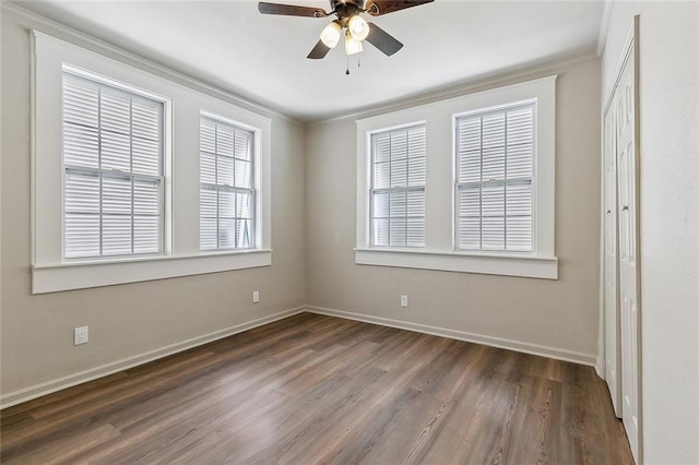 empty room with a ceiling fan, dark wood-style flooring, crown molding, and baseboards