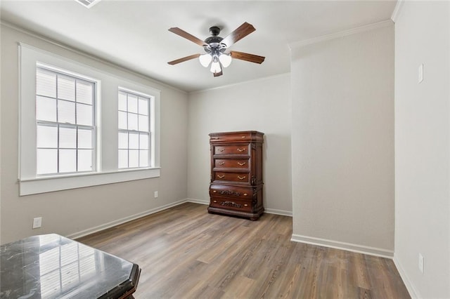 interior space with a ceiling fan, crown molding, baseboards, and wood finished floors