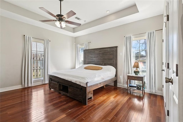 bedroom with wood-type flooring, visible vents, a raised ceiling, and baseboards