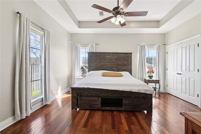 bedroom featuring dark wood-type flooring, a raised ceiling, and baseboards