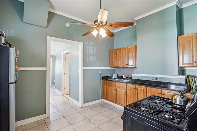 kitchen with black gas range, a ceiling fan, freestanding refrigerator, a sink, and light tile patterned flooring