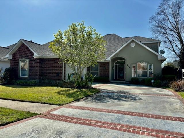 view of front of house featuring decorative driveway, brick siding, and a front lawn