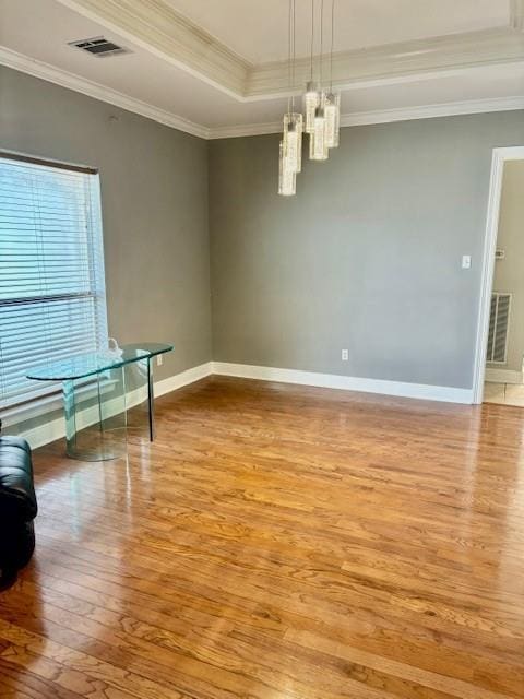 unfurnished room with baseboards, visible vents, hardwood / wood-style flooring, ornamental molding, and a tray ceiling