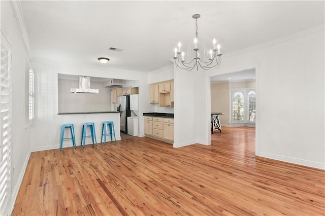 kitchen featuring visible vents, freestanding refrigerator, wall chimney exhaust hood, dark countertops, and crown molding