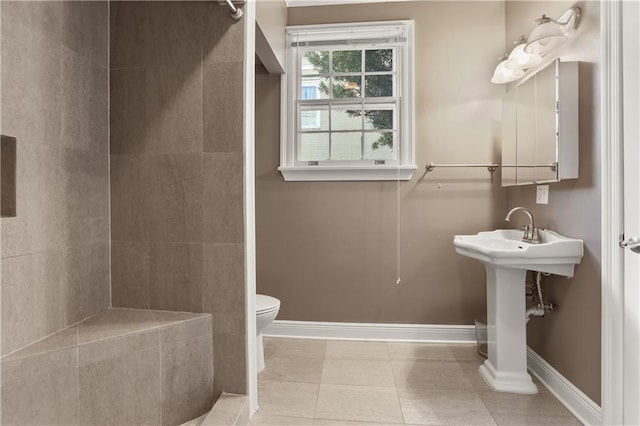 bathroom with toilet, a sink, baseboards, a tile shower, and tile patterned floors