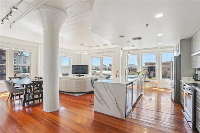 kitchen with a center island with sink, dark wood finished floors, light stone countertops, stainless steel appliances, and a sink