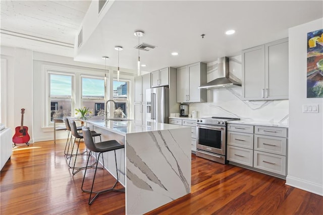 kitchen with gray cabinetry, stainless steel appliances, a sink, visible vents, and wall chimney exhaust hood