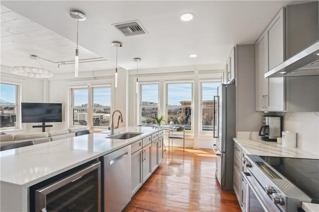 kitchen with beverage cooler, visible vents, wall chimney exhaust hood, stainless steel appliances, and a sink