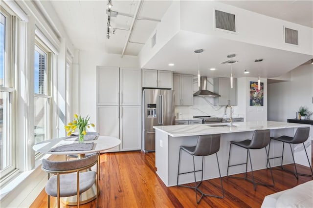 kitchen featuring stainless steel appliances, wall chimney exhaust hood, a sink, and visible vents