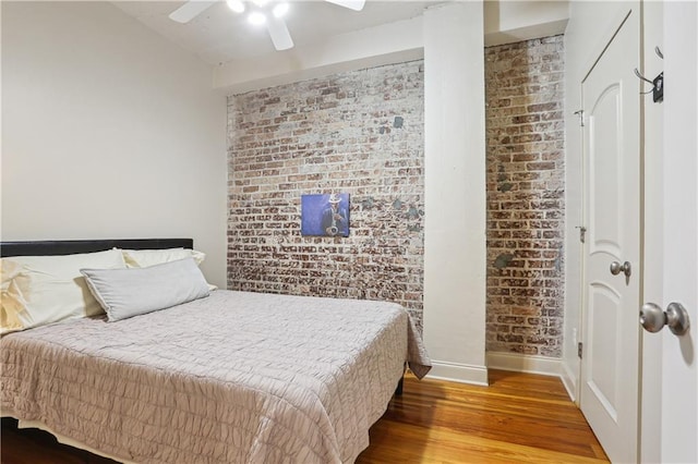 bedroom featuring brick wall, baseboards, ceiling fan, and wood finished floors