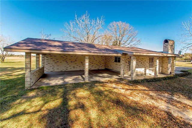 back of house with a carport, brick siding, a lawn, and a chimney