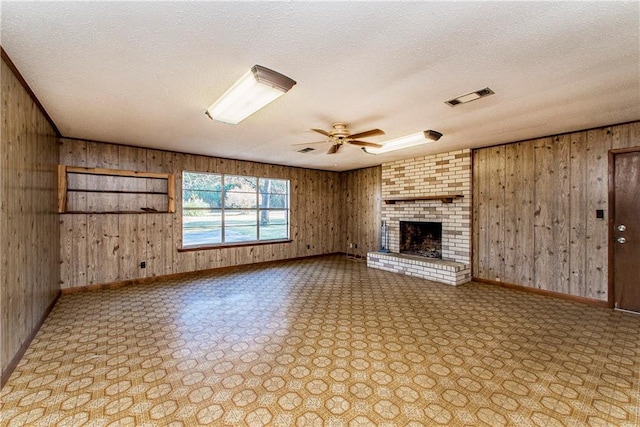 unfurnished living room featuring visible vents, a brick fireplace, ceiling fan, wood walls, and tile patterned floors