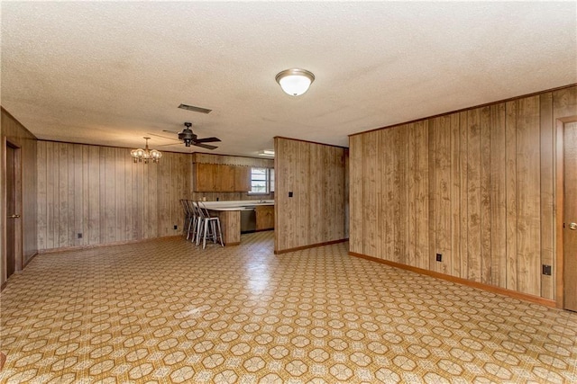 unfurnished living room featuring baseboards, visible vents, wooden walls, and a textured ceiling