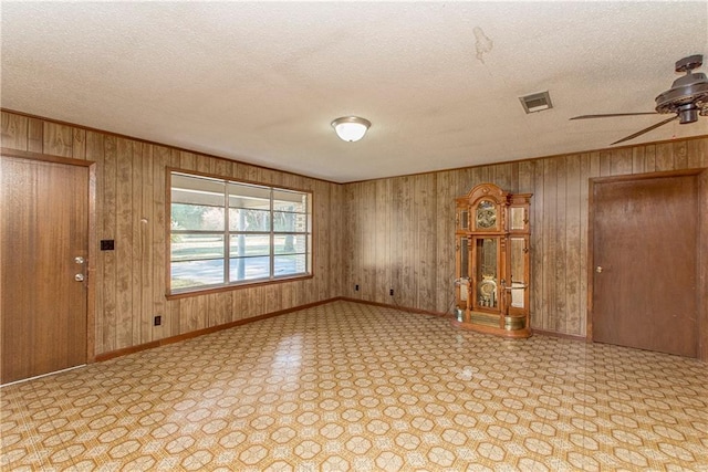 empty room featuring wooden walls, visible vents, a textured ceiling, and baseboards