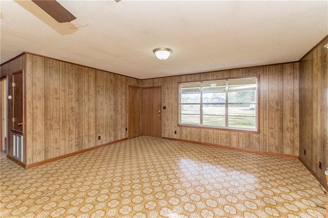 empty room featuring wooden walls, baseboards, and a textured ceiling