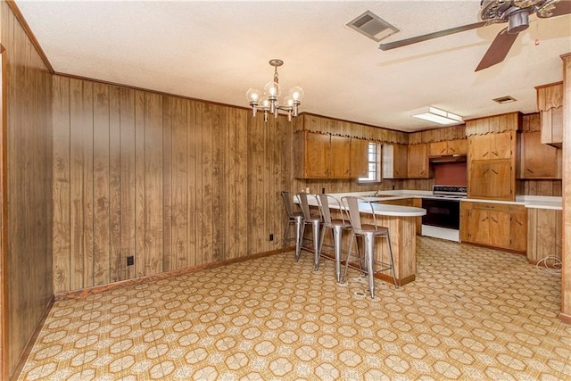 kitchen with light countertops, range with electric cooktop, visible vents, and wooden walls