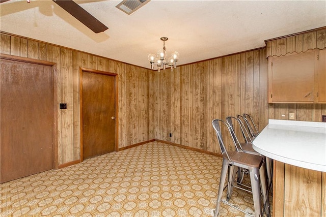 unfurnished dining area with baseboards, visible vents, crown molding, wood walls, and ceiling fan with notable chandelier