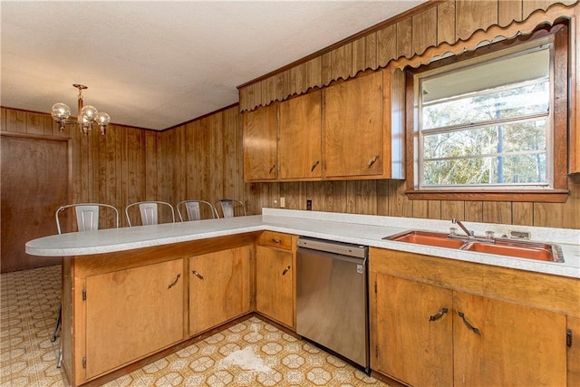 kitchen with light countertops, dishwasher, wooden walls, and a sink