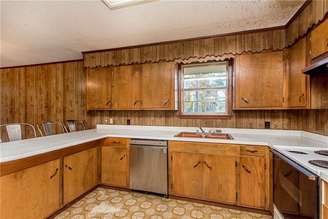kitchen featuring brown cabinets, light countertops, stainless steel dishwasher, a sink, and wood walls