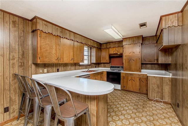 kitchen featuring brown cabinetry, under cabinet range hood, electric range oven, and light floors