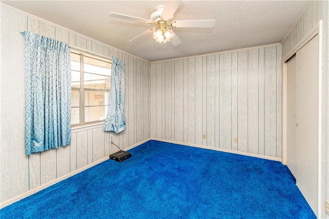 empty room featuring a textured ceiling, wood walls, carpet flooring, and a ceiling fan