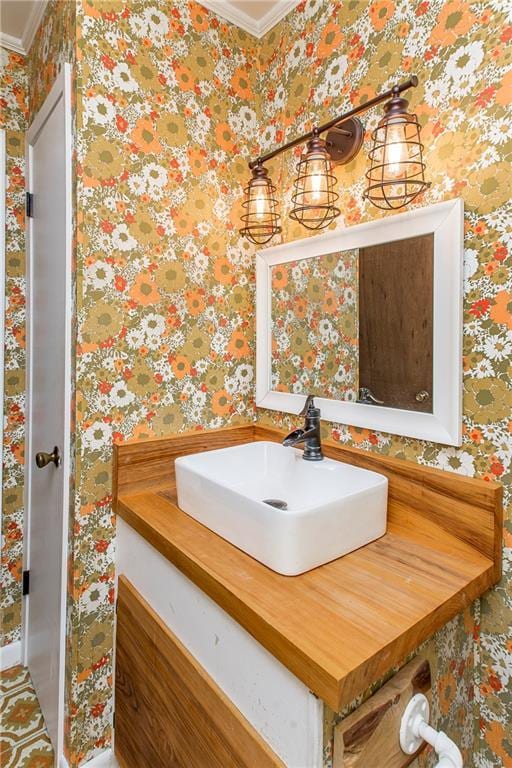 bathroom featuring ornamental molding, a sink, and wallpapered walls