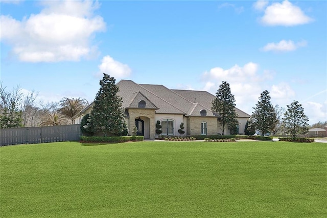 french country inspired facade with stone siding, fence, and a front yard