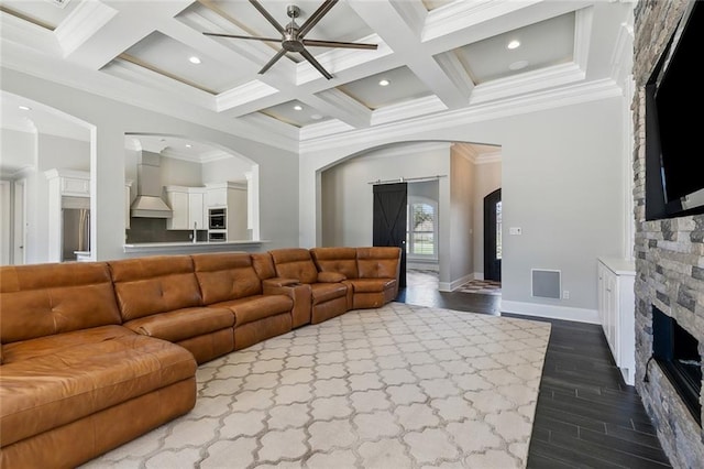 living room with arched walkways, dark wood-type flooring, beamed ceiling, and a stone fireplace