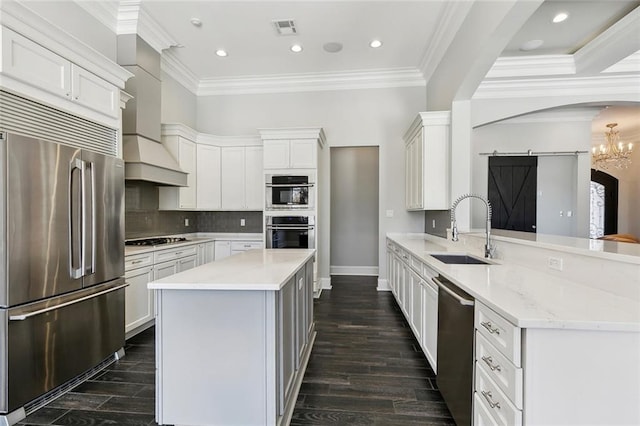 kitchen featuring a barn door, arched walkways, a peninsula, stainless steel appliances, and a sink