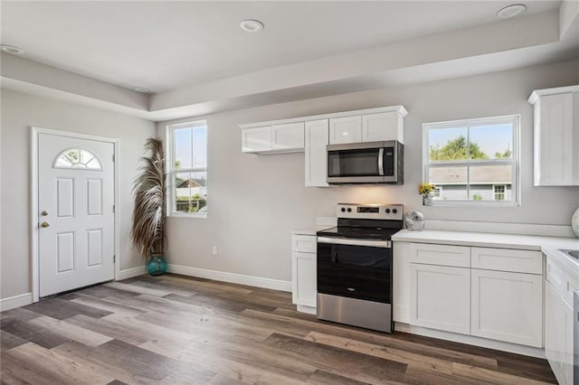 kitchen with appliances with stainless steel finishes, white cabinets, baseboards, and wood finished floors