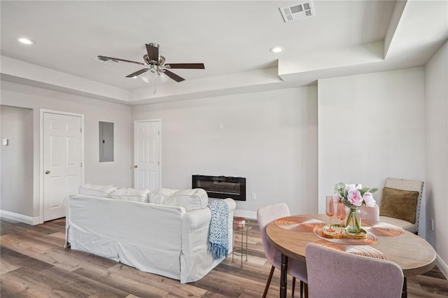 living area with wood finished floors, visible vents, baseboards, a tray ceiling, and a glass covered fireplace