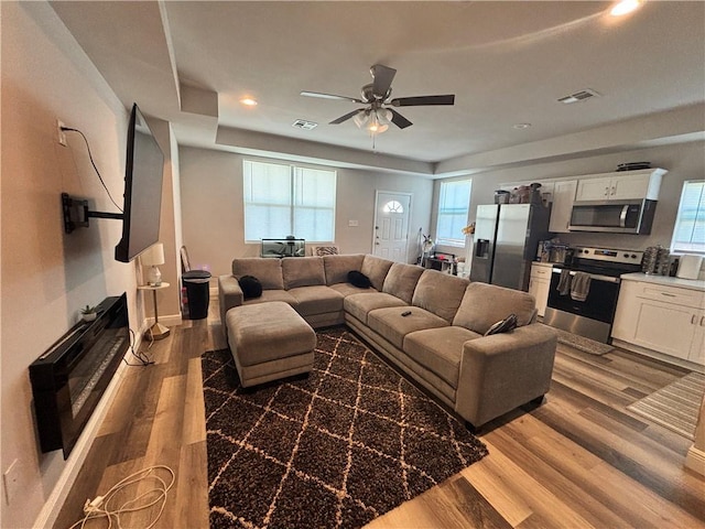 living room with light wood-style flooring, visible vents, ceiling fan, and baseboards