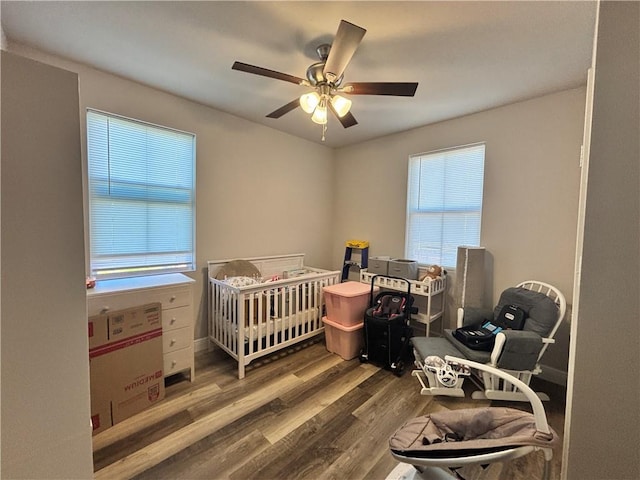 bedroom featuring a nursery area, a ceiling fan, and wood finished floors