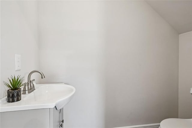 bathroom with lofted ceiling, vanity, toilet, and baseboards