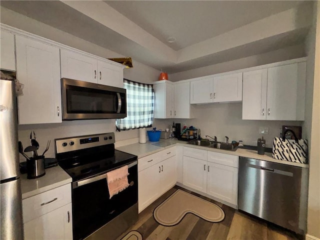 kitchen featuring a raised ceiling, dark wood-style floors, appliances with stainless steel finishes, white cabinetry, and a sink