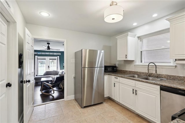 kitchen featuring dark countertops, appliances with stainless steel finishes, white cabinetry, a sink, and light tile patterned flooring