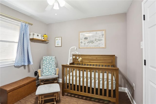 bedroom with a nursery area, ceiling fan, baseboards, and wood finished floors