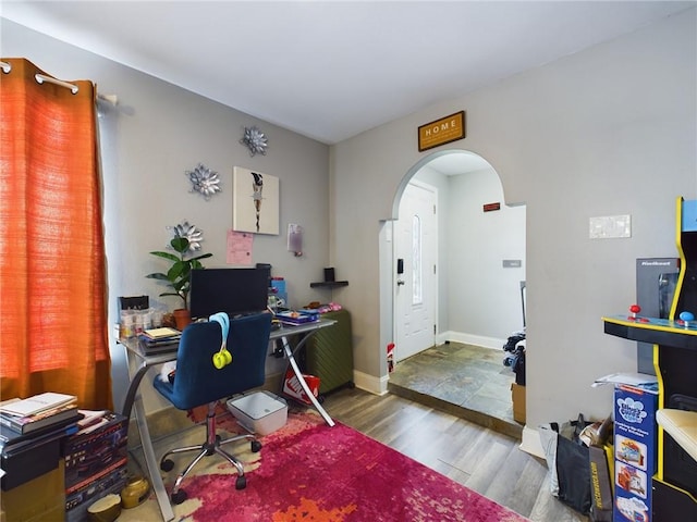 office area with arched walkways, wood finished floors, and baseboards