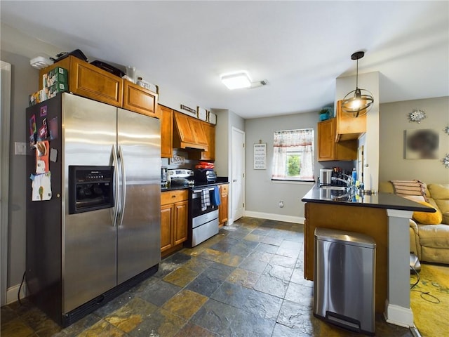 kitchen featuring baseboards, dark countertops, stainless steel appliances, stone tile flooring, and a sink