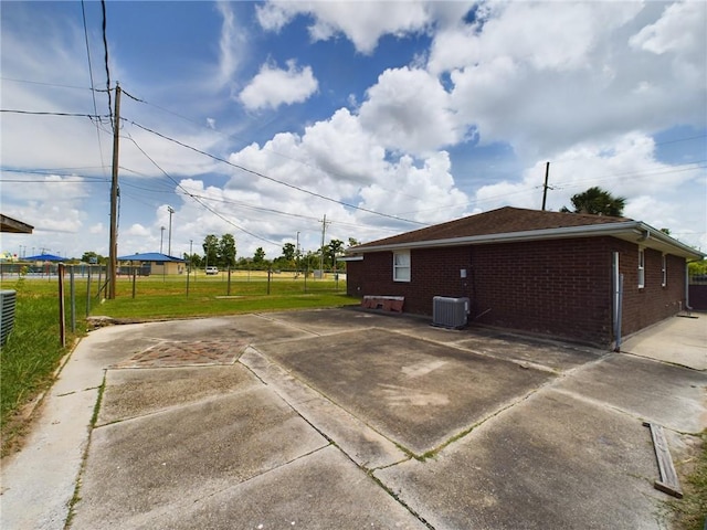 exterior space with a yard, brick siding, central AC unit, and fence