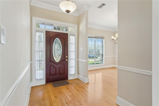 foyer with a wealth of natural light, visible vents, an inviting chandelier, and crown molding