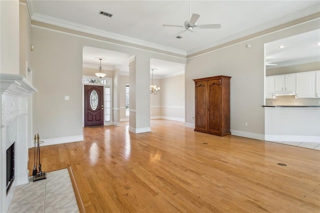 unfurnished living room featuring visible vents, a fireplace, ornamental molding, ceiling fan with notable chandelier, and light wood-type flooring