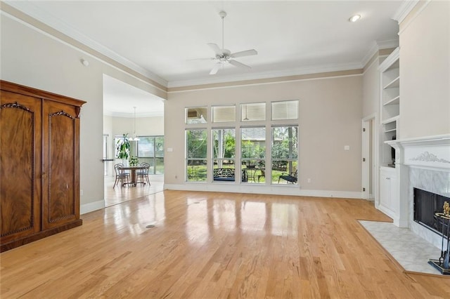 unfurnished living room with light wood finished floors, ceiling fan, built in features, a premium fireplace, and ornamental molding