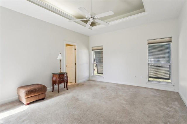 carpeted empty room featuring a raised ceiling, a ceiling fan, and baseboards