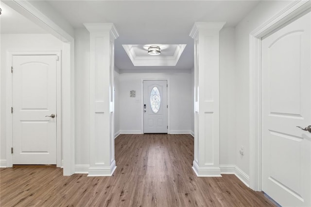 foyer entrance featuring a tray ceiling, crown molding, ornate columns, wood finished floors, and baseboards