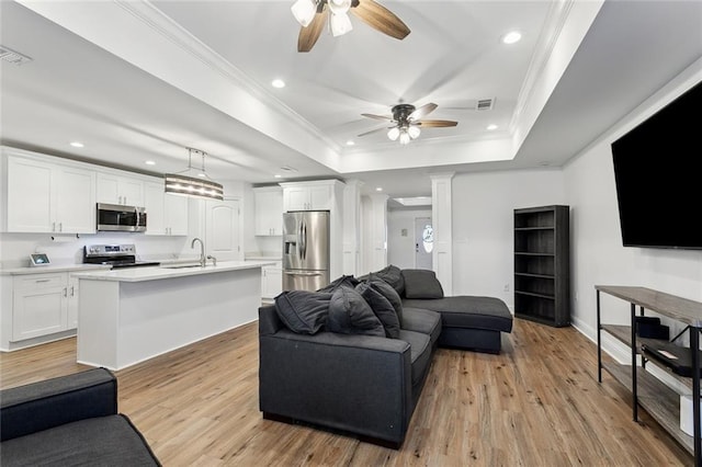 living area with a tray ceiling, recessed lighting, light wood-style floors, and crown molding