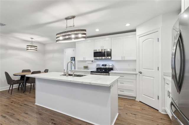 kitchen featuring a center island with sink, white cabinets, appliances with stainless steel finishes, wood finished floors, and a sink