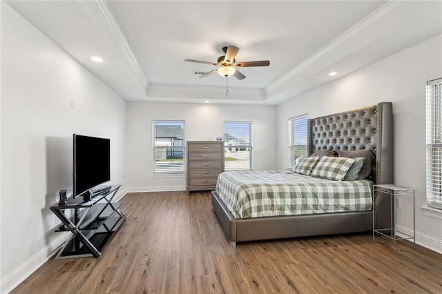 bedroom with a raised ceiling, crown molding, baseboards, and wood finished floors