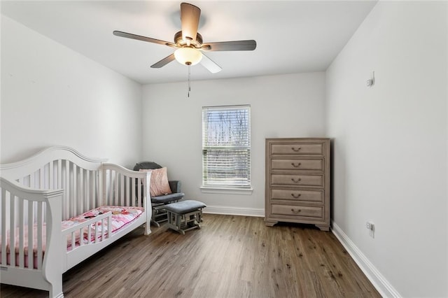 bedroom with ceiling fan, a crib, baseboards, and wood finished floors